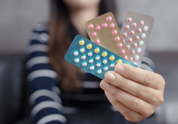 Woman in faded in background holding birth control pill packets in foreground